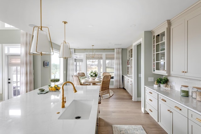 kitchen with sink, light stone countertops, decorative backsplash, decorative light fixtures, and light wood-type flooring