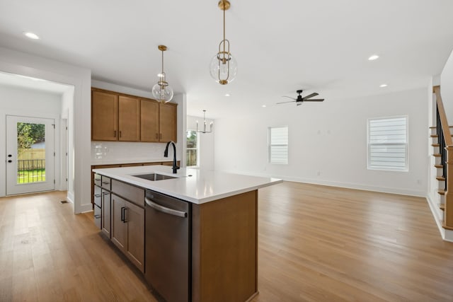 kitchen featuring ceiling fan with notable chandelier, an island with sink, stainless steel dishwasher, hanging light fixtures, and sink