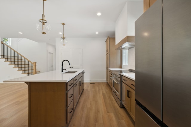 kitchen with stainless steel appliances, light hardwood / wood-style floors, sink, an island with sink, and pendant lighting