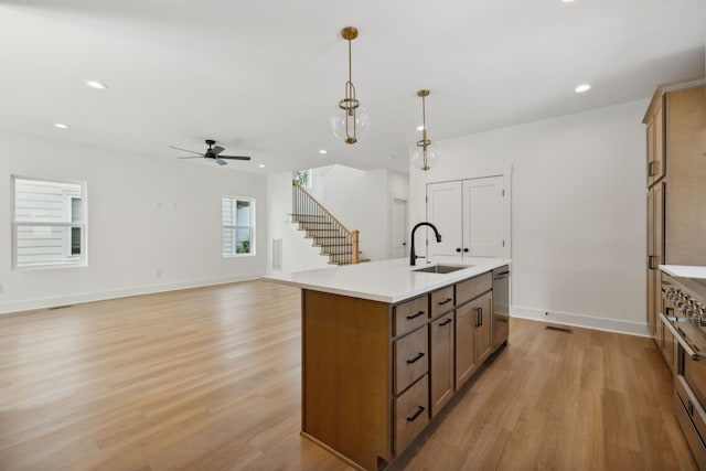 kitchen with a kitchen island with sink, light hardwood / wood-style flooring, decorative light fixtures, and sink