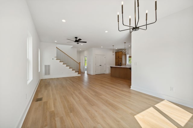 unfurnished living room featuring ceiling fan with notable chandelier and light hardwood / wood-style floors