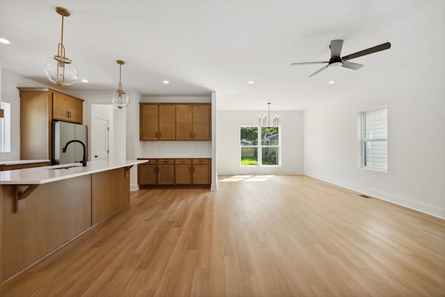 kitchen with pendant lighting, sink, ceiling fan with notable chandelier, and light wood-type flooring