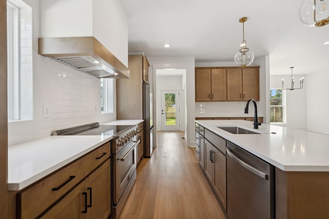 kitchen featuring a healthy amount of sunlight, pendant lighting, appliances with stainless steel finishes, and wall chimney exhaust hood