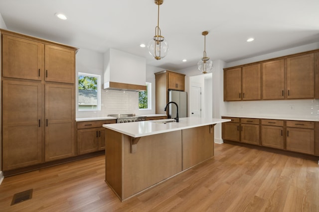 kitchen featuring a center island with sink, light hardwood / wood-style flooring, stainless steel fridge, and decorative light fixtures