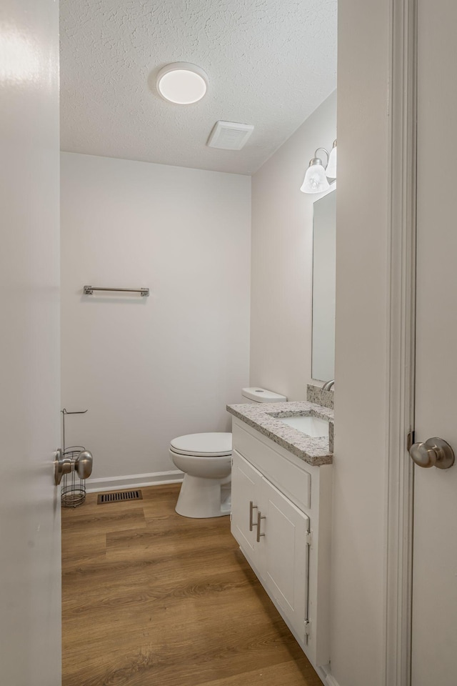 half bathroom featuring vanity, wood finished floors, baseboards, a textured ceiling, and toilet