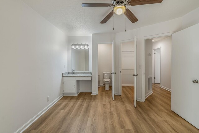 unfurnished bedroom with light hardwood / wood-style flooring, sink, ceiling fan, connected bathroom, and a textured ceiling