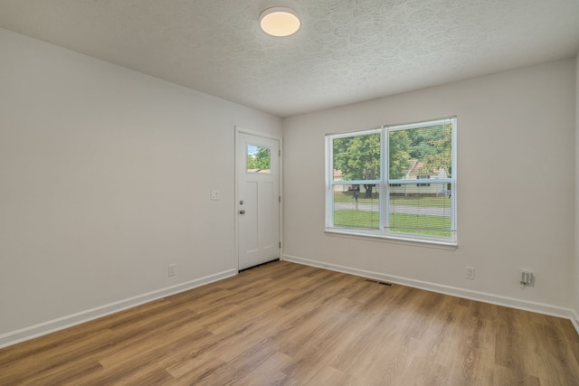 unfurnished room with a textured ceiling, a healthy amount of sunlight, and light hardwood / wood-style flooring