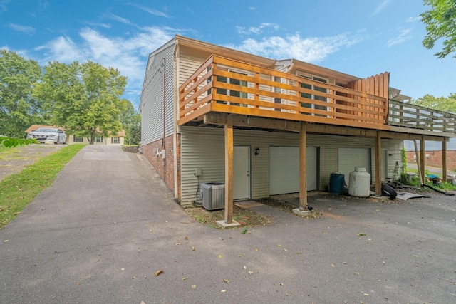 exterior space with a deck, aphalt driveway, cooling unit, a garage, and brick siding