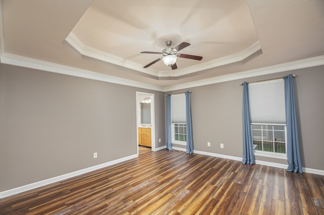 empty room featuring dark hardwood / wood-style floors, a tray ceiling, ornamental molding, and ceiling fan