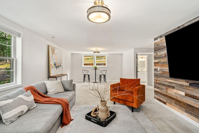 living area featuring light carpet, a healthy amount of sunlight, and wood walls