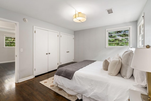 bedroom with visible vents, multiple windows, two closets, and dark wood-type flooring