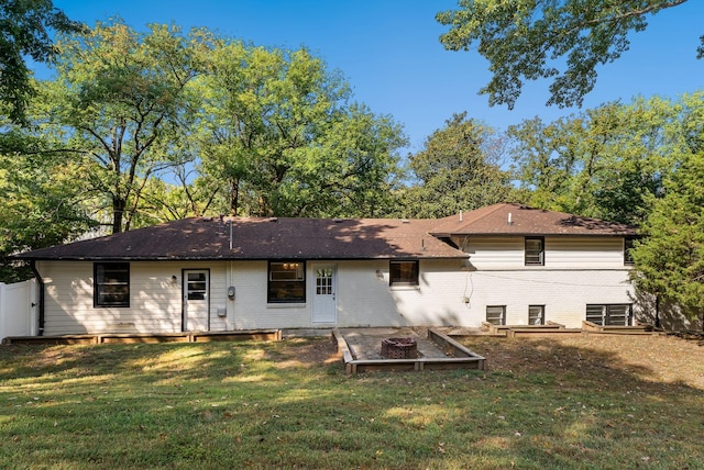 rear view of house with brick siding, a fire pit, a yard, and fence