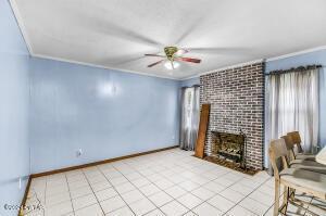 unfurnished living room featuring a brick fireplace, crown molding, baseboards, ceiling fan, and light tile patterned floors