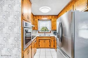 kitchen with brown cabinets, a sink, stainless steel appliances, light tile patterned flooring, and light countertops