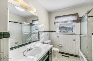 bathroom featuring vanity, bath / shower combo with glass door, tile patterned floors, toilet, and tile walls