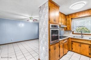 kitchen with brown cabinetry, light tile patterned floors, oven, and black electric stovetop