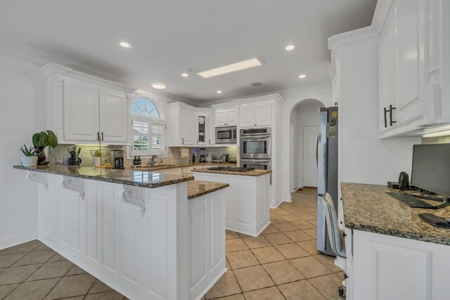 kitchen with dark stone countertops, crown molding, light tile patterned floors, kitchen peninsula, and appliances with stainless steel finishes