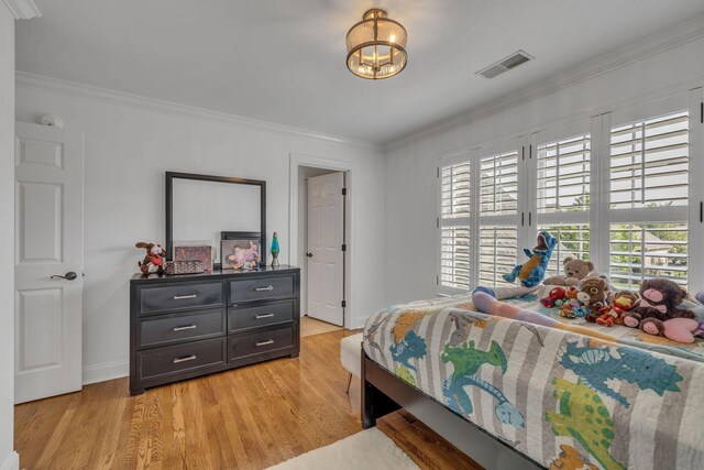 bedroom featuring ornamental molding, light wood-type flooring, and an inviting chandelier