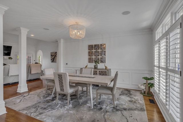 dining space featuring decorative columns, crown molding, wood-type flooring, and a notable chandelier