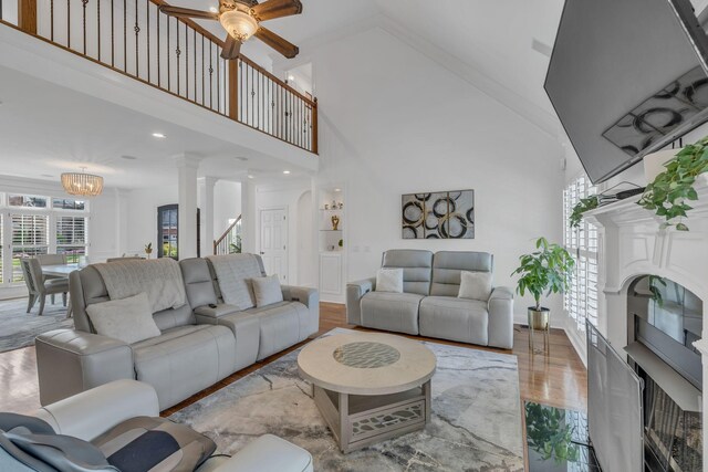 living room with ceiling fan with notable chandelier, high vaulted ceiling, decorative columns, and light hardwood / wood-style floors