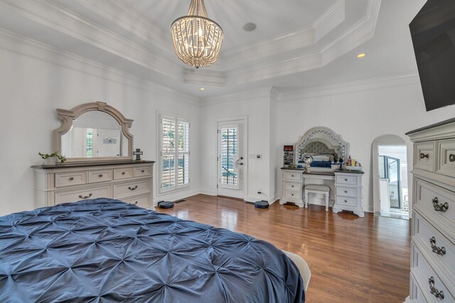 bedroom featuring built in desk, ornamental molding, wood-type flooring, access to exterior, and a raised ceiling