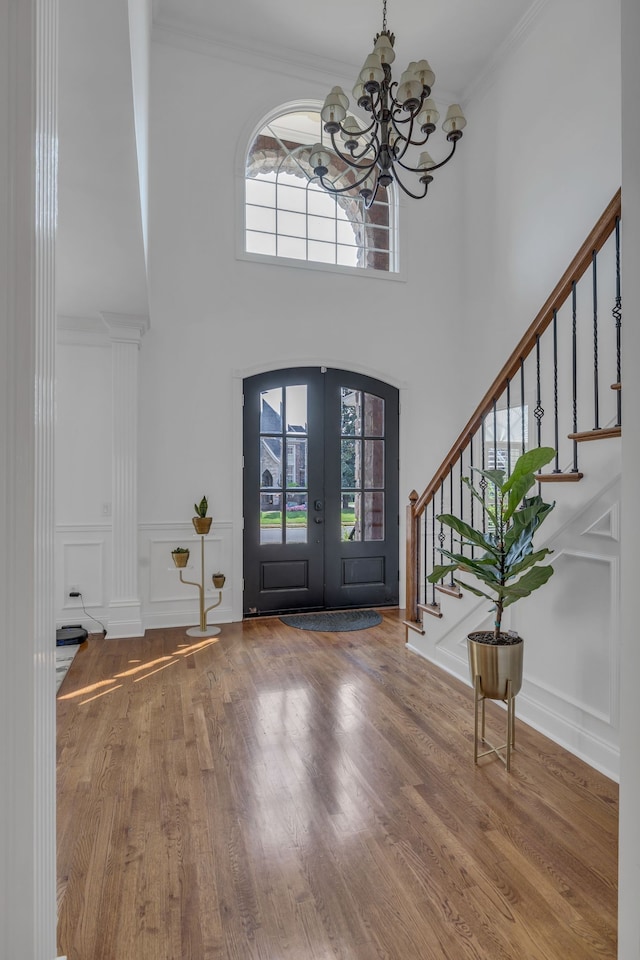 entrance foyer with a high ceiling, a notable chandelier, crown molding, french doors, and hardwood / wood-style flooring