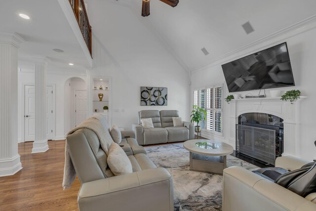 living room with wood-type flooring, ceiling fan, ornamental molding, and high vaulted ceiling