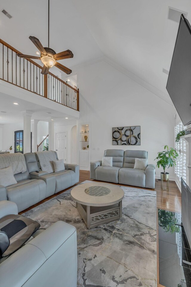 living room with a high ceiling, wood-type flooring, ceiling fan, and decorative columns