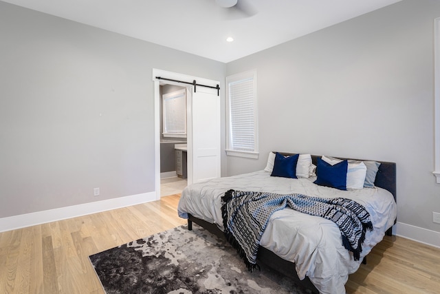 bedroom with a barn door, ceiling fan, light hardwood / wood-style floors, and ensuite bathroom