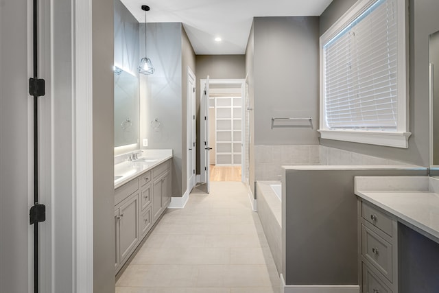 bathroom featuring tile patterned flooring, tiled bath, and vanity