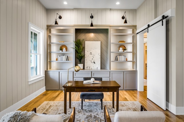 office space featuring a barn door, light wood-type flooring, and wooden walls