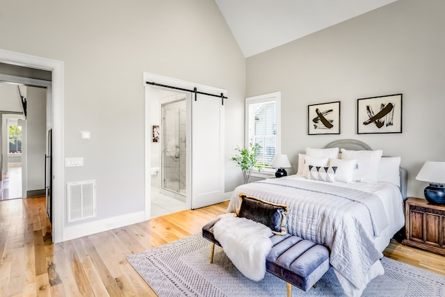 bedroom featuring a barn door, ensuite bath, high vaulted ceiling, and light wood-type flooring