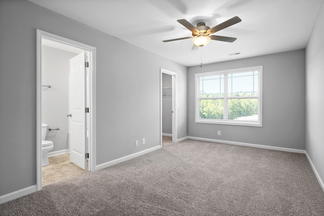 unfurnished bedroom featuring a spacious closet, a closet, ensuite bathroom, light carpet, and ceiling fan