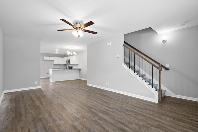 unfurnished living room with stairway, visible vents, baseboards, dark wood-style flooring, and ceiling fan with notable chandelier