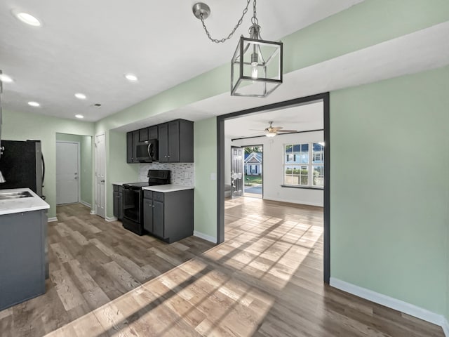 kitchen with backsplash, light wood-type flooring, ceiling fan with notable chandelier, stainless steel appliances, and pendant lighting