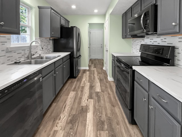 kitchen with gray cabinetry, sink, black appliances, wood-type flooring, and tasteful backsplash