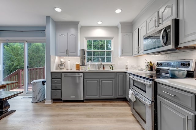 kitchen with gray cabinetry, light hardwood / wood-style flooring, backsplash, appliances with stainless steel finishes, and sink