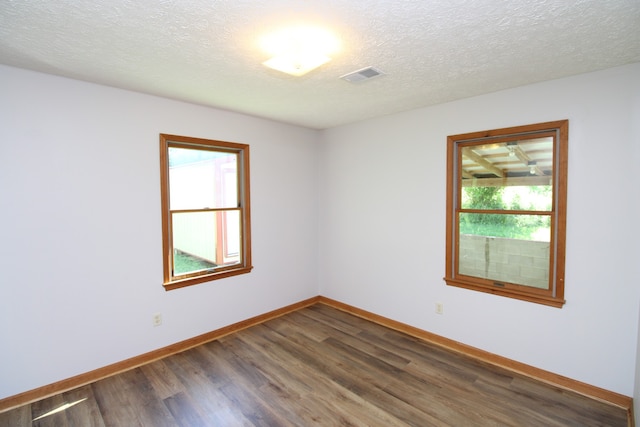 empty room with dark wood-type flooring, a textured ceiling, and plenty of natural light