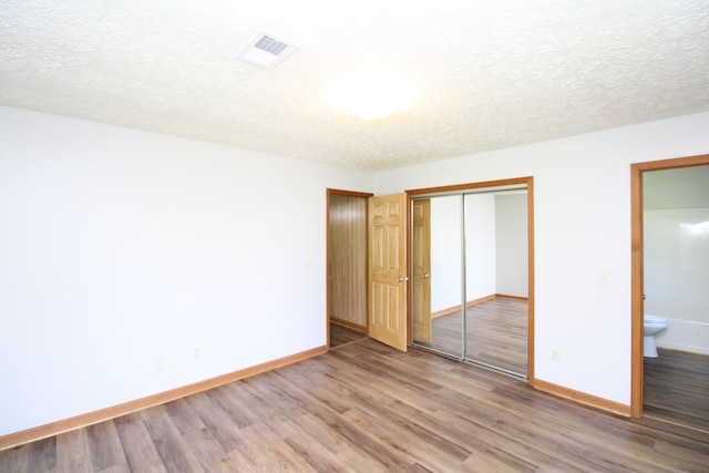 unfurnished bedroom with a closet, wood-type flooring, ensuite bathroom, and a textured ceiling