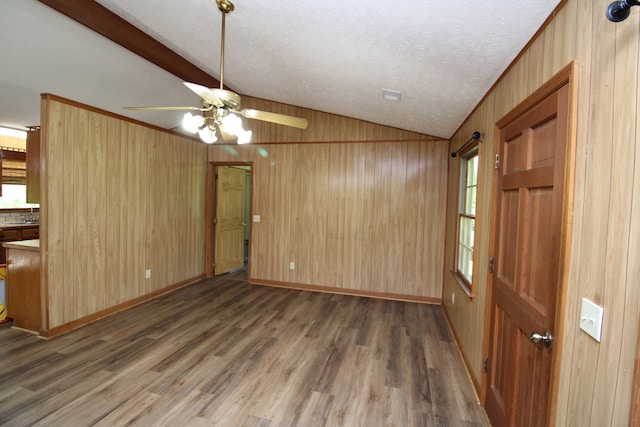 interior space with dark wood-type flooring, wood walls, ceiling fan, and a textured ceiling