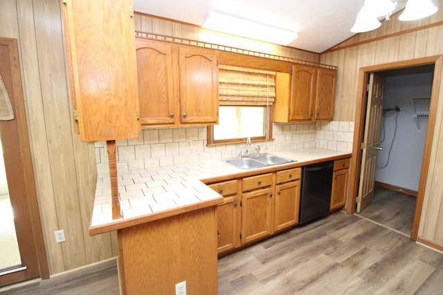 kitchen featuring backsplash, wood walls, dishwasher, sink, and light hardwood / wood-style floors