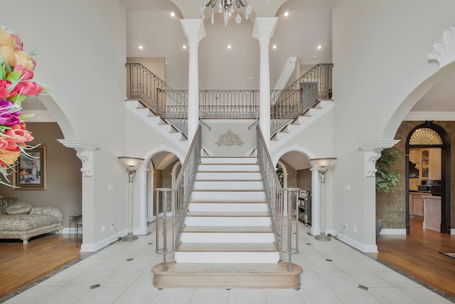 stairway featuring a towering ceiling, wood-type flooring, and decorative columns