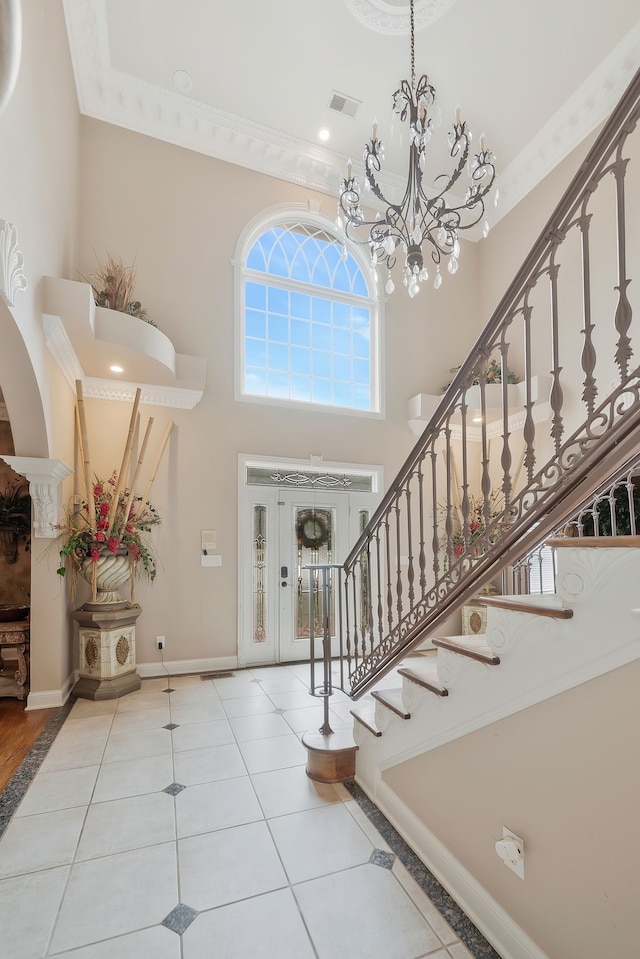 foyer entrance with light wood-type flooring, a chandelier, crown molding, and a towering ceiling