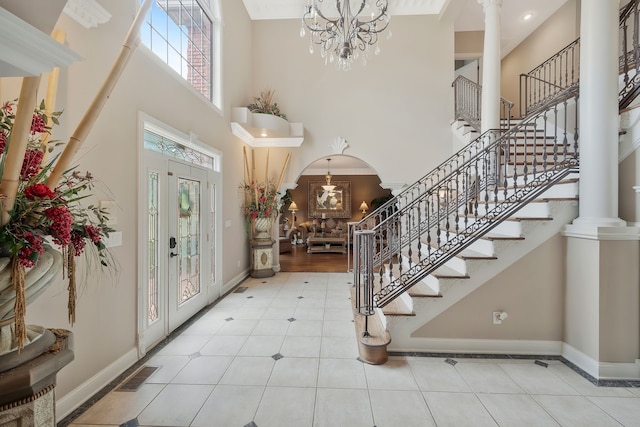 tiled foyer with decorative columns, a wealth of natural light, a notable chandelier, and a towering ceiling