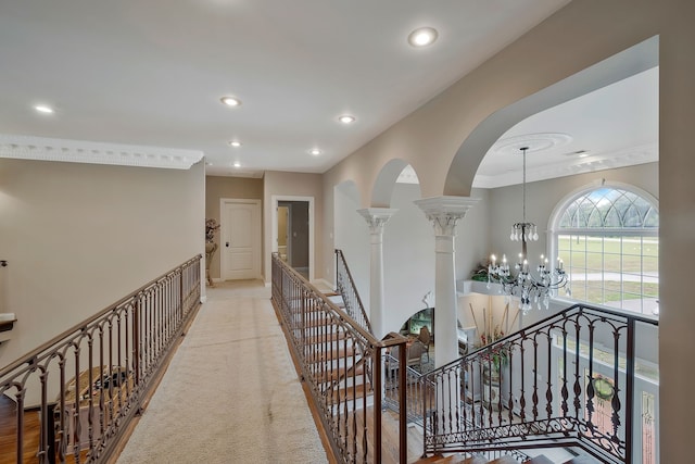 corridor with a notable chandelier, light carpet, and decorative columns