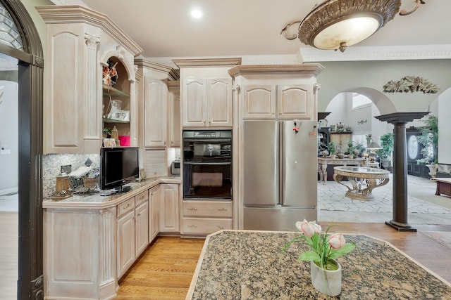 kitchen with stainless steel refrigerator, backsplash, decorative columns, black double oven, and light hardwood / wood-style floors