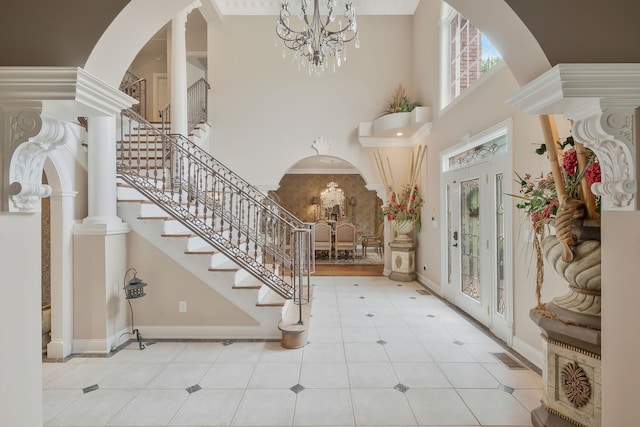 tiled foyer entrance featuring a notable chandelier, a towering ceiling, and decorative columns