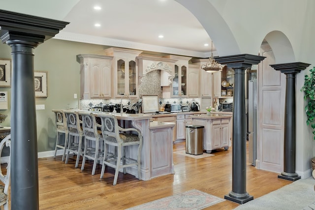 kitchen featuring light wood-type flooring, kitchen peninsula, a kitchen breakfast bar, a kitchen island, and decorative backsplash