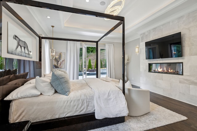 bedroom featuring hardwood / wood-style floors, a tile fireplace, a raised ceiling, and ornamental molding