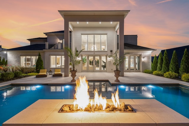 pool at dusk featuring an outdoor fire pit, a patio area, and french doors